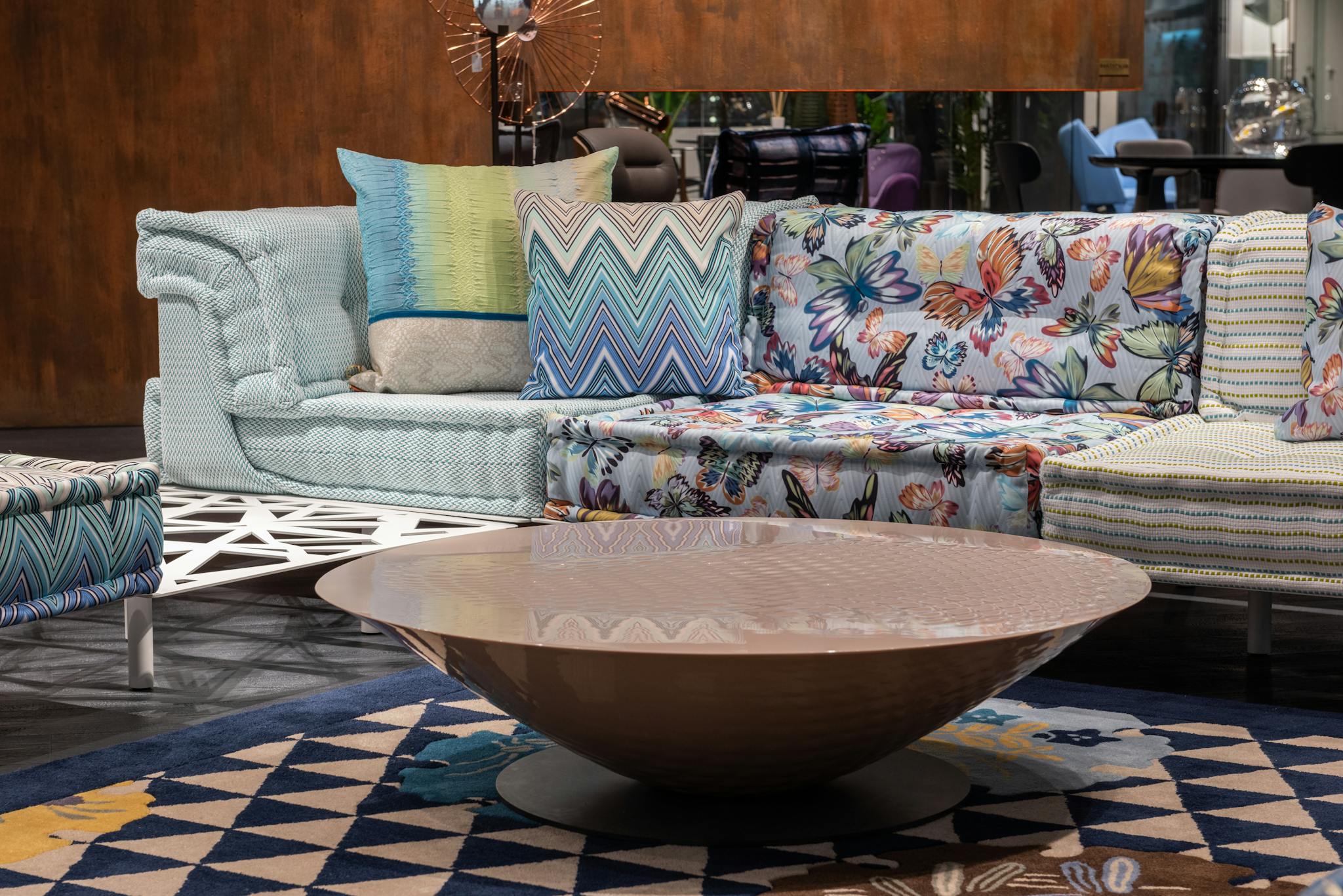 Comfortable sofa with colorful cushions placed near modern table on rug in contemporary living room of spacious apartment with pouf